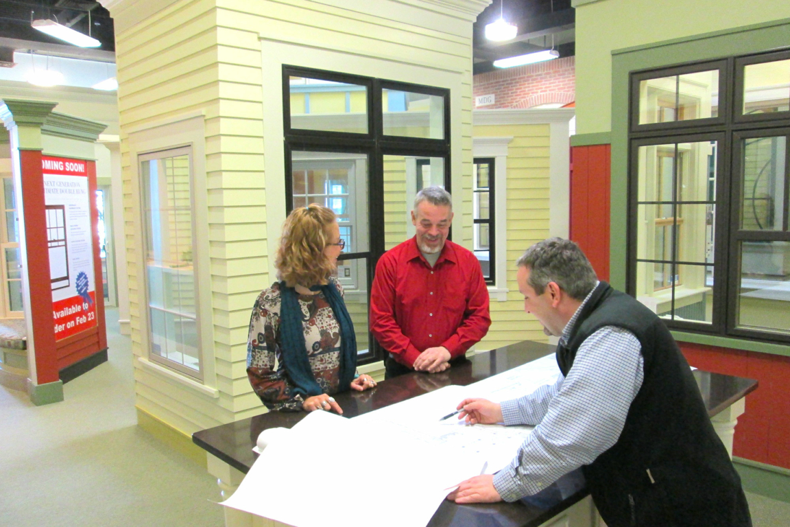A man and woman smile while looking over blueprints for a new home construction design.