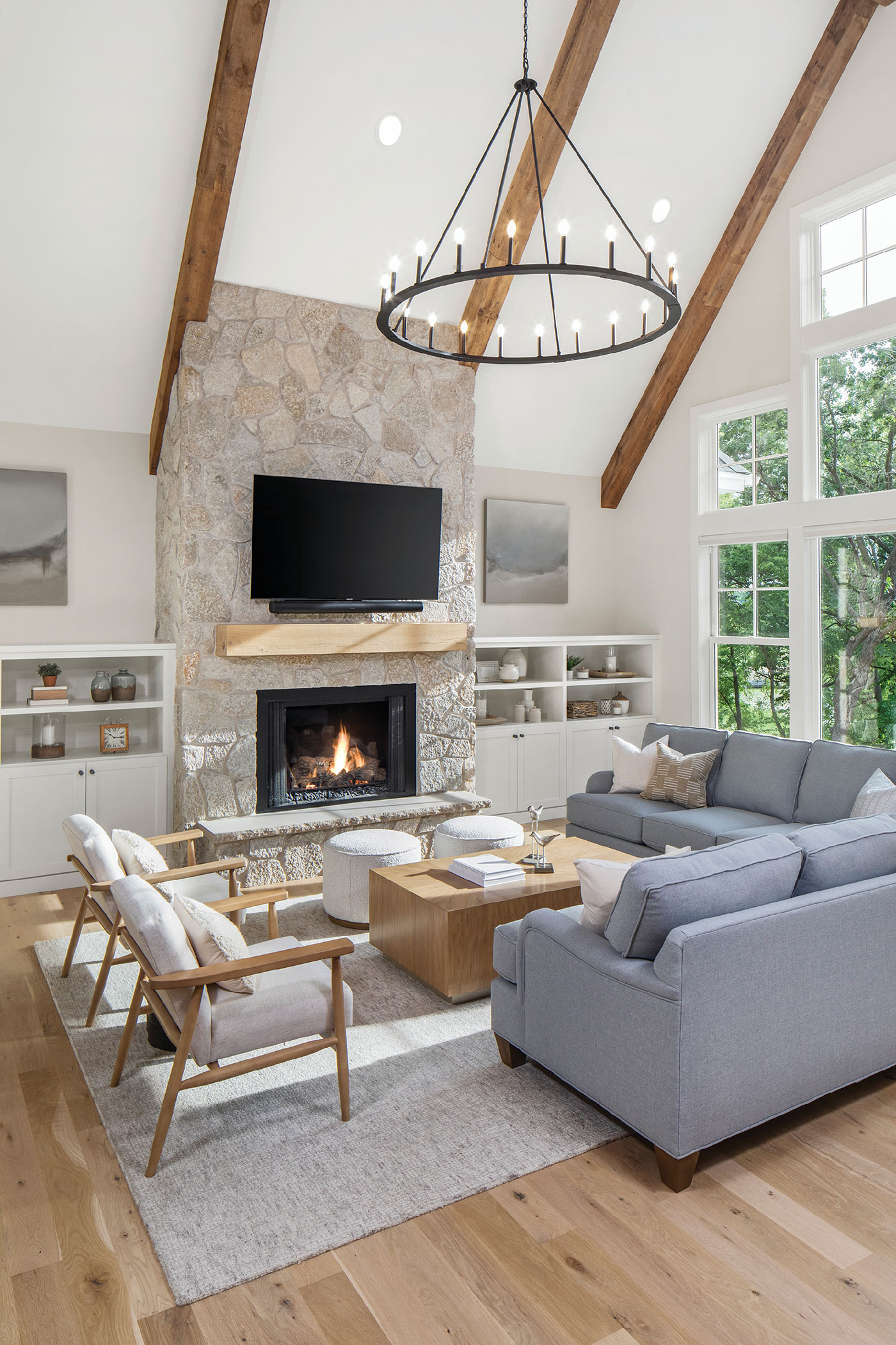 large windows flank a far wall in cathedral ceilinged family room with fireplace