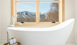 A large bathtub sits below two large double-hung windows