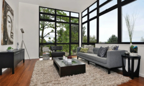 A set of large, black framed windows anchor the corner of a light and bright living room.