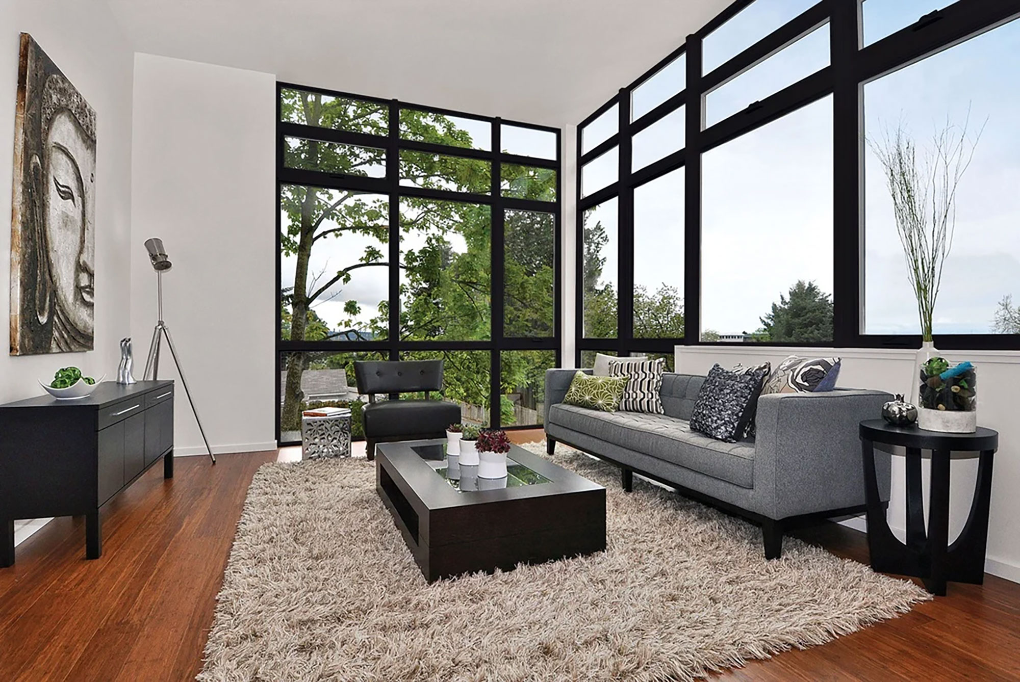 A set of large, black framed windows anchor the corner of a light and bright living room.