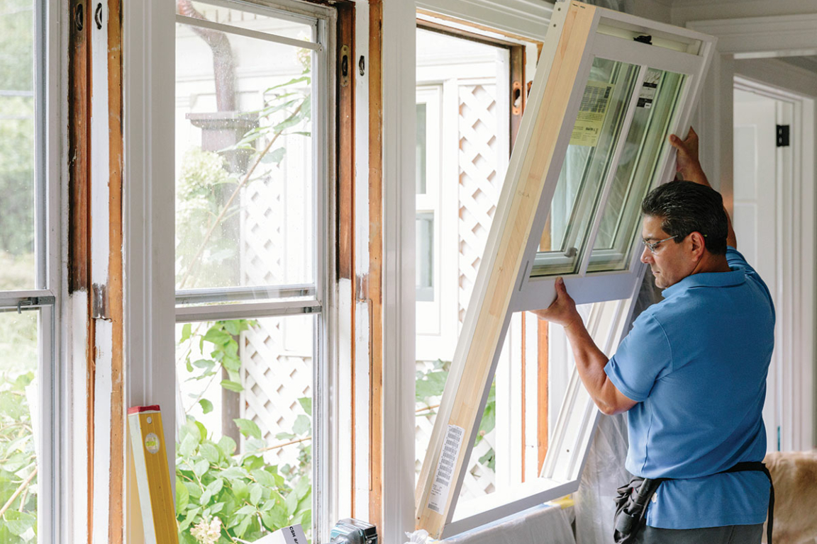 A man carefully places a window into a new construction opening.