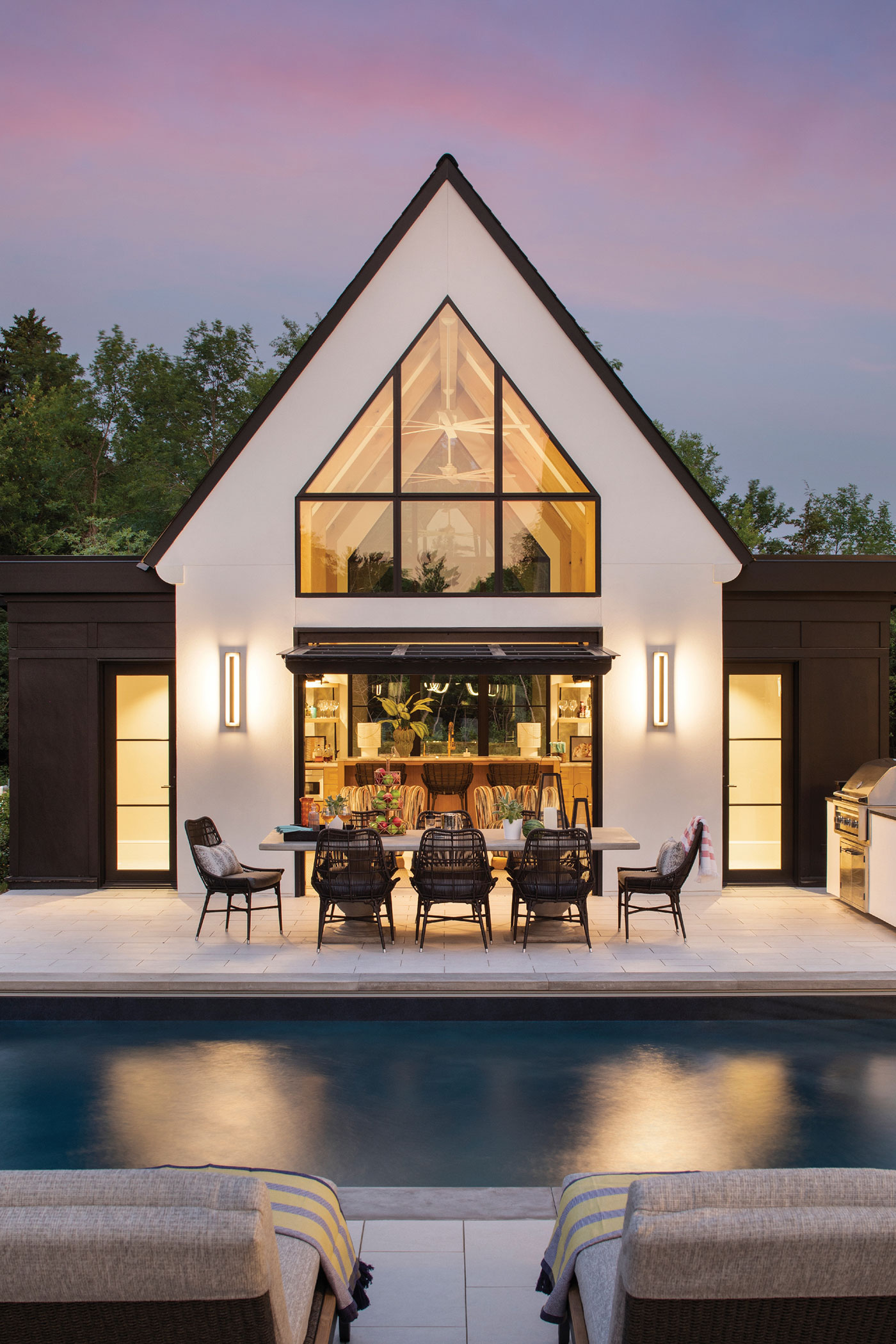 A cathedral style window on a contemporary out building by a pool at night