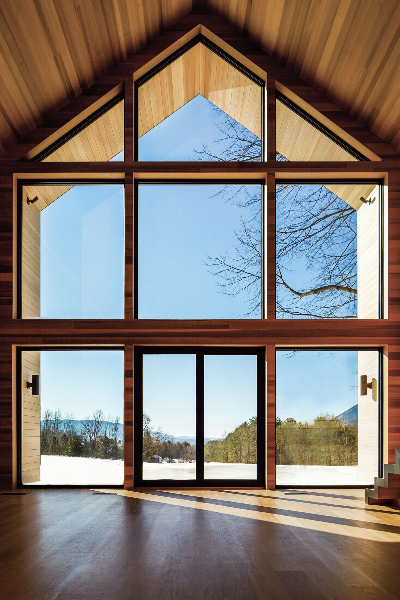 a grid of wooden windows and doors fill a full two story wall of a home