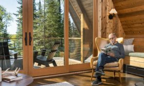 A man sits in a sunlit family room with angular windows and doors filling a A frame home