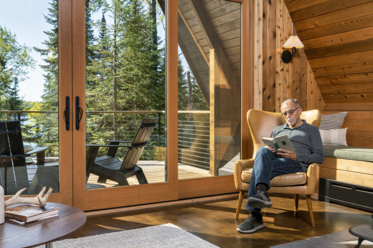 A man sits in a sunlit family room with angular windows and doors filling a A frame home